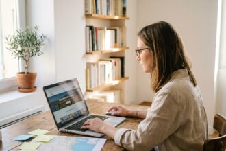 Femme cherchant un appartement avec terrasse à Nice sur son ordinateur portable depuis un bureau à domicile organisé